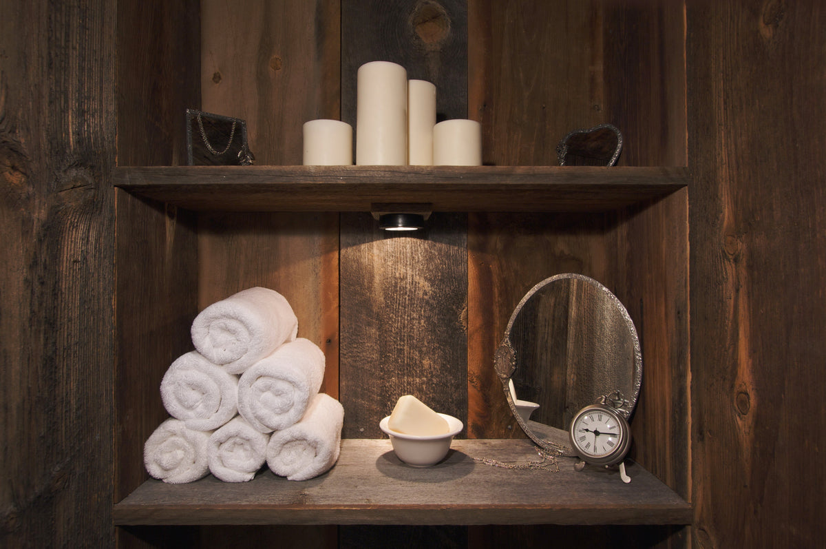 Rolled white towels, soap, a mirror and candles on dark wooden shelves.