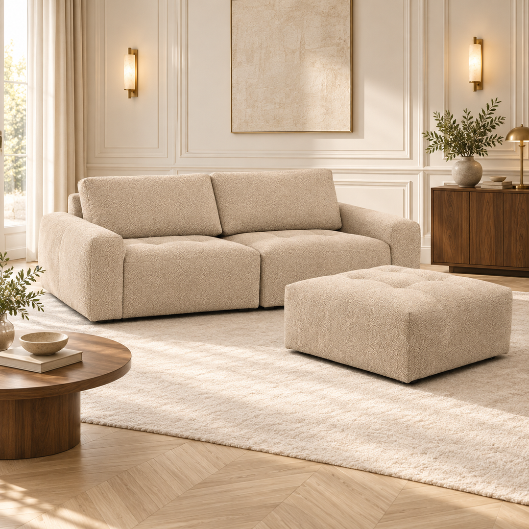 Beige Madele-soffa med två sittdelar och en djuphäftad puff i ett vardagsrum med väggpaneler och en mörk träskänk.