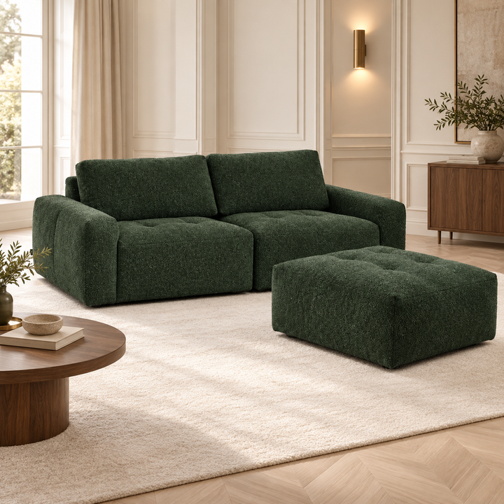 Mörkgrön Madele-soffa med två sittdelar och fristående puff på en ljus matta intill ett högt fönster.