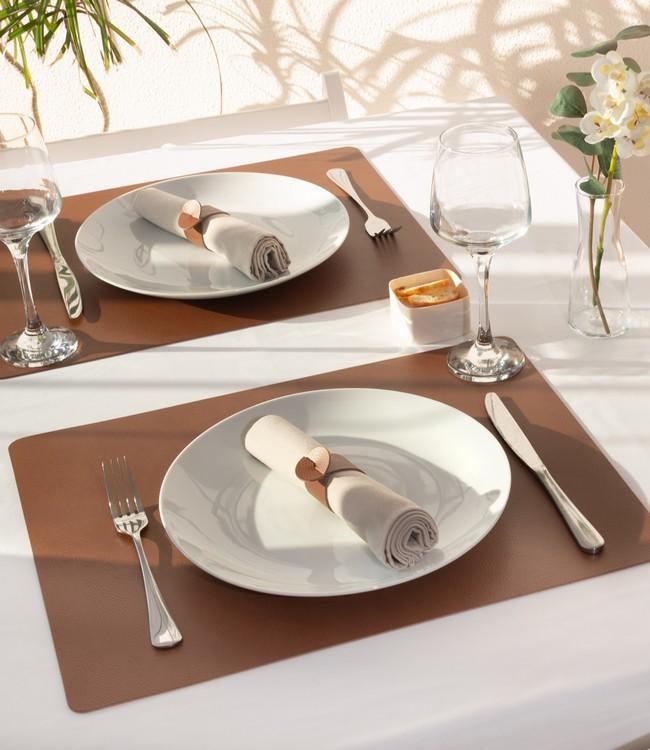 Finesse placemats in dark brown beneath white plates and cloth napkins on a set table