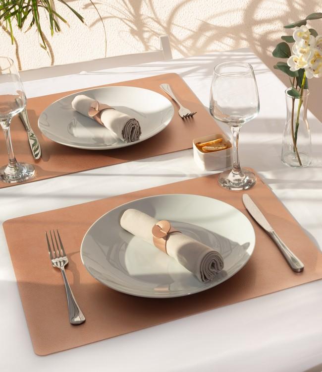 Finesse placemats in cognac brown beneath white plates and cloth napkins on a set table