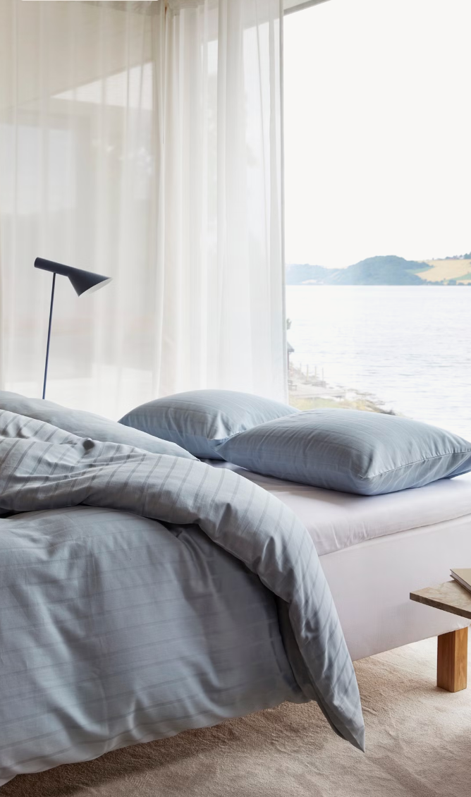 Light blue Høie Milano duvet cover set on a made bed in a bedroom; subtle tonal stripes