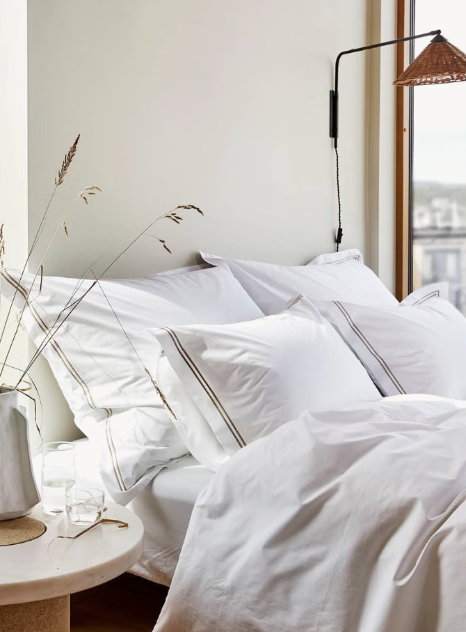 White Høie Paris bedding on a bed with double golden-brown border stripes on the pillowcases