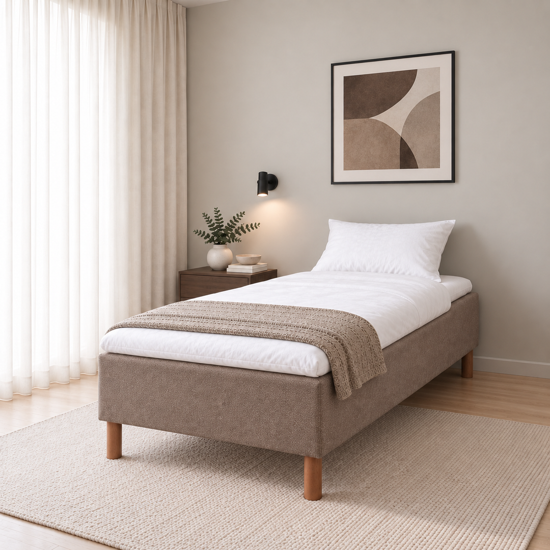 Hotel Basic Pocket runkosänky 100x200 cm, Sawana 25 ruskea modernissa makuuhuoneessa viistosti jalkopäästä kuvattuna. Sisustushavainnekuva; Hotel Plus -petauspatja sisältyy hintaan, vuodevaatteet eivät.