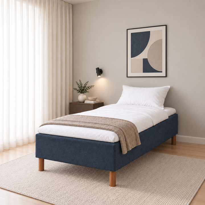 Hotel Basic Pocket runkosänky 100x200 cm, Sawana 80 sininen modernissa makuuhuoneessa viistosti jalkopäästä kuvattuna. Sisustushavainnekuva; Hotel Plus -petauspatja sisältyy hintaan, vuodevaatteet eivät.