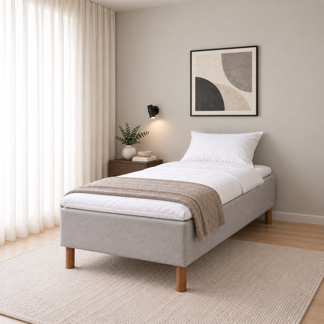 Hotel Basic Pocket runkosänky 100x200 cm, Vogue 14 vaaleanharmaa modernissa makuuhuoneessa viistosti jalkopäästä kuvattuna. Sisustushavainnekuva; Hotel Plus -petauspatja sisältyy hintaan, vuodevaatteet eivät.