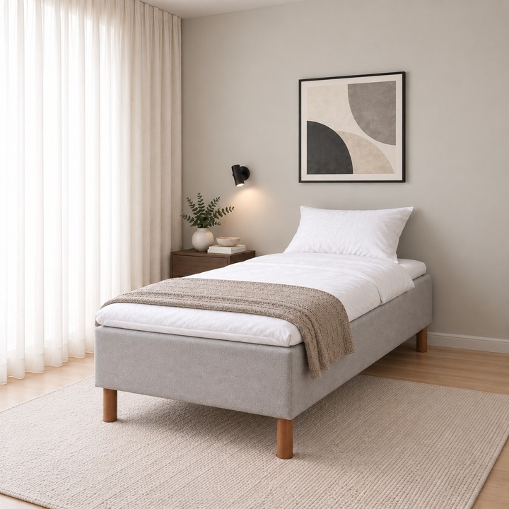 Hotel Basic Pocket runkosänky 100x200 cm, Vogue 14 vaaleanharmaa modernissa makuuhuoneessa viistosti jalkopäästä kuvattuna. Sisustushavainnekuva; Hotel Plus -petauspatja sisältyy hintaan, vuodevaatteet eivät.