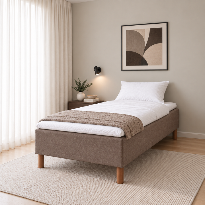 Hotel Basic Pocket runkosänky 120x200 cm, Sawana 25 ruskea modernissa makuuhuoneessa viistosti jalkopäästä kuvattuna. Sisustushavainnekuva; Hotel Plus -petauspatja sisältyy hintaan, vuodevaatteet eivät.