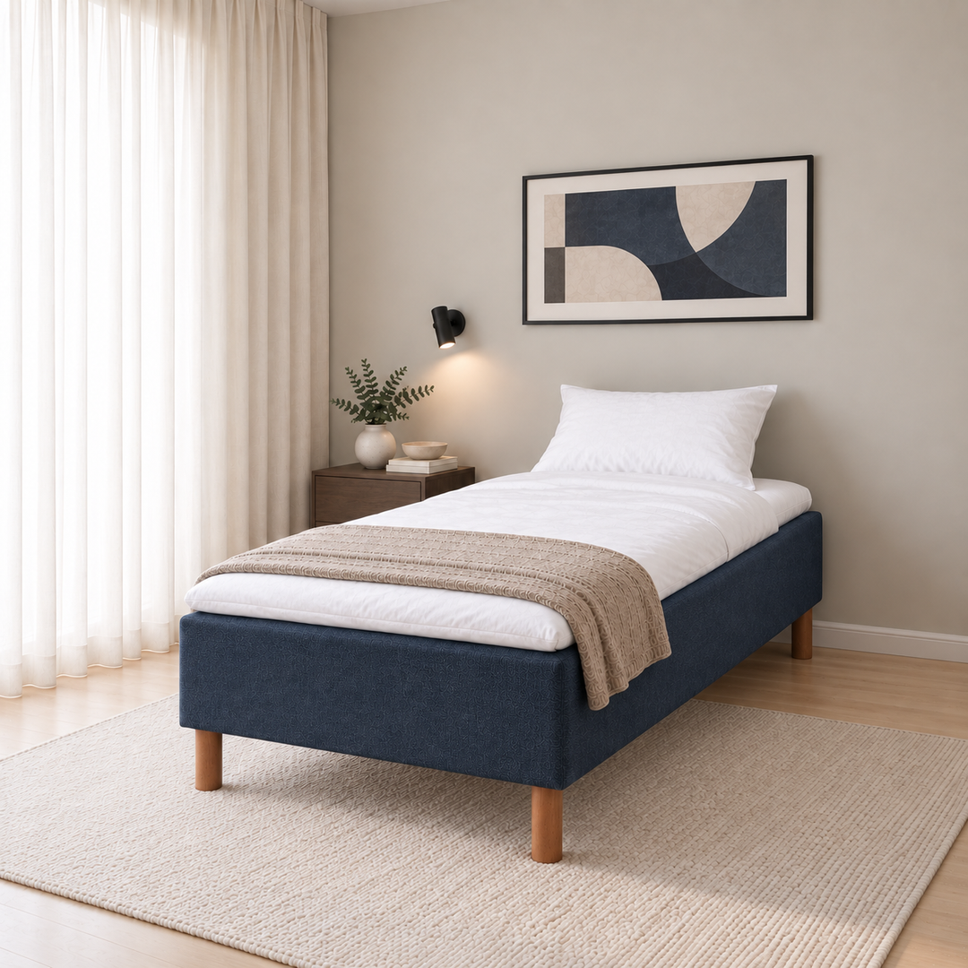 Hotel Basic Pocket runkosänky 90x200 cm, Sawana 80 sininen modernissa makuuhuoneessa viistosti jalkopäästä kuvattuna. Sisustushavainnekuva; Hotel Plus -petauspatja sisältyy hintaan, vuodevaatteet eivät.
