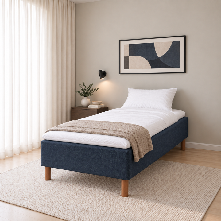 Hotel Basic Pocket runkosänky 90x200 cm, Sawana 80 sininen modernissa makuuhuoneessa viistosti jalkopäästä kuvattuna. Sisustushavainnekuva; Hotel Plus -petauspatja sisältyy hintaan, vuodevaatteet eivät.