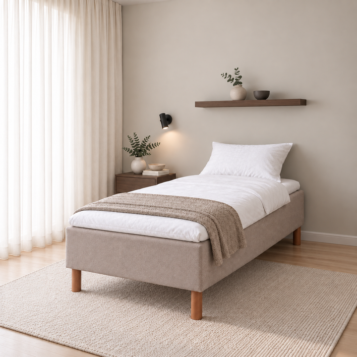 Hotel Basic Pocket runkosänky 90x200 cm, Thomas 03 beige modernissa makuuhuoneessa viistosti jalkopäästä kuvattuna. Sisustushavainnekuva; Hotel Plus -petauspatja sisältyy hintaan, vuodevaatteet eivät.