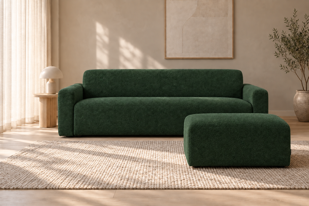 Mörkgrön Heta-soffa och matchande rektangulär sittpuff på en ljus matta, med solljus från vänster.