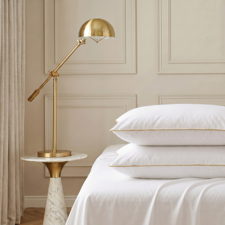 Two white Hotel Luxus large pillows with gold piping stacked on a bed