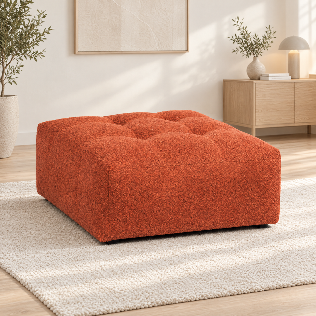 Orangeröd Madele-sittpuff med djuphäftad ovansida på en ljus matta i ett ljust vardagsrum.