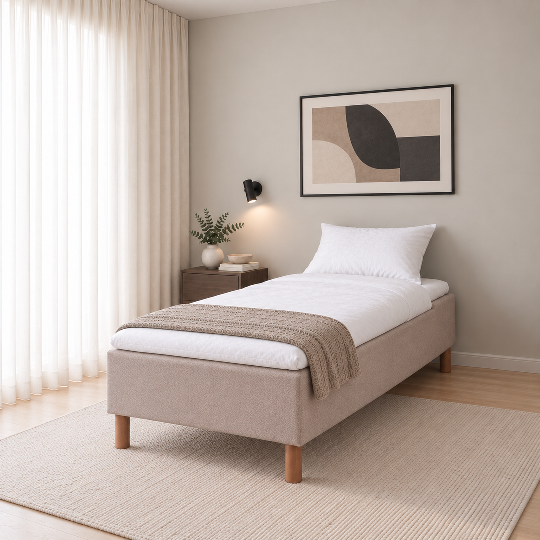 Hotel Luxus Pocket Bonnel runkosänky 90x200 cm, Thomas 03 beige modernissa makuuhuoneessa viistosti jalkopäästä kuvattuna. Sisustushavainnekuva; Hotel Plus -petauspatja sisältyy hintaan, vuodevaatteet eivät.