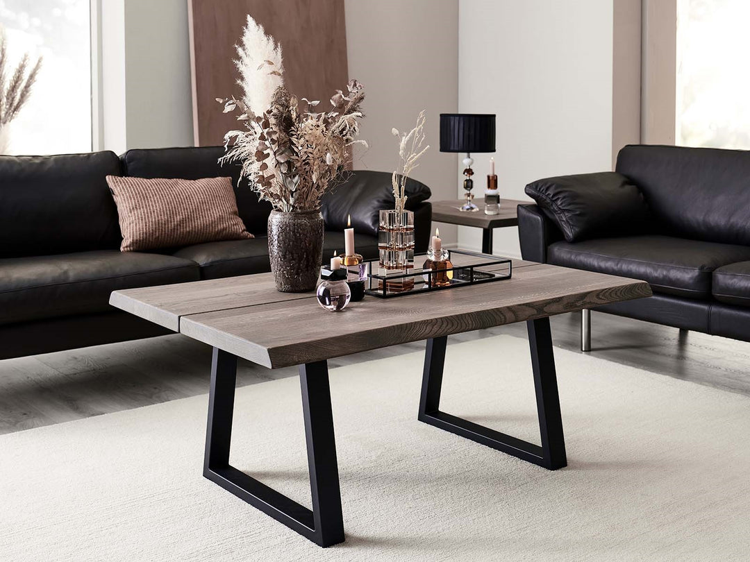 Ruskea sohvapöytä mustilla Trapez Sofa Base -kehysjaloilla mustien sohvien edessä