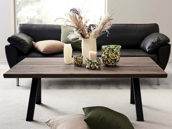 Ruskea sohvapöytä mustilla VS Coffee Table -jaloilla mustan sohvan edessä