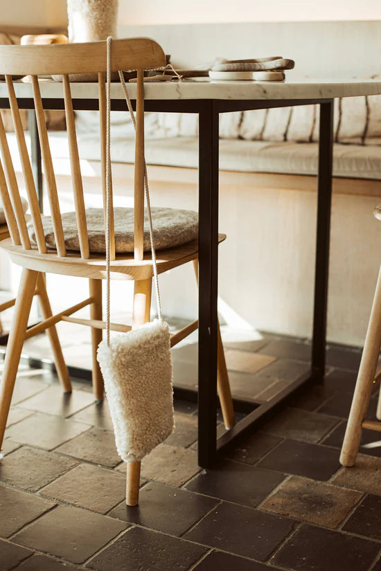 White KYWIE phone pouch hanging from a wooden chair back beside a dining table