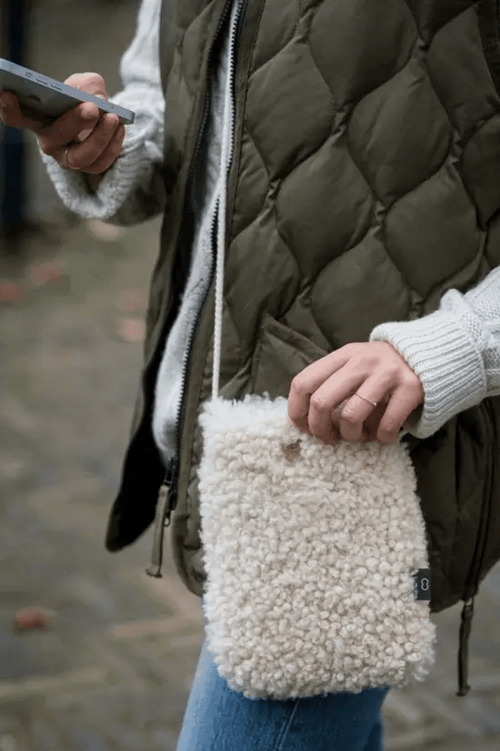 White KYWIE phone pouch worn across a person's body with a hand at the opening