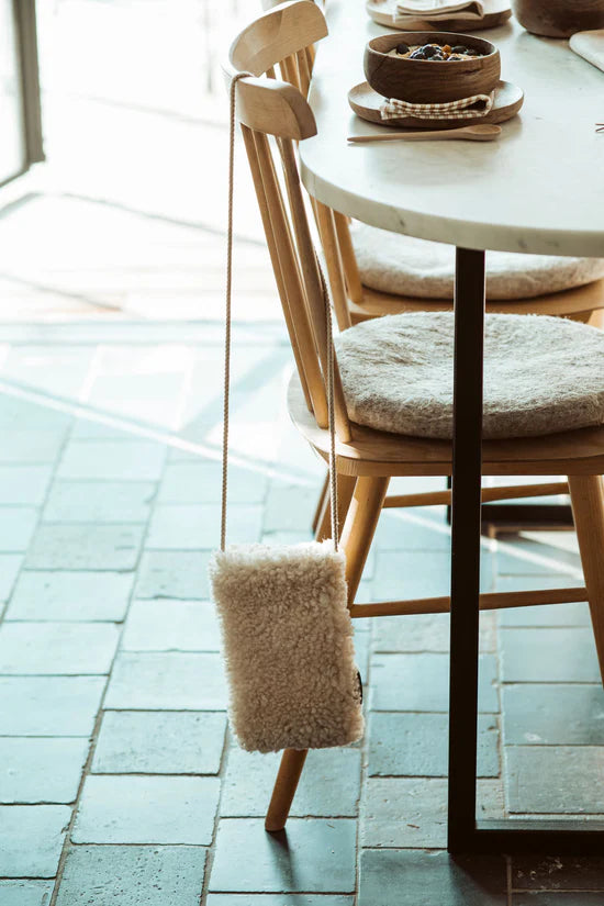 White KYWIE phone pouch hanging from a wooden chair back in a bright dining area