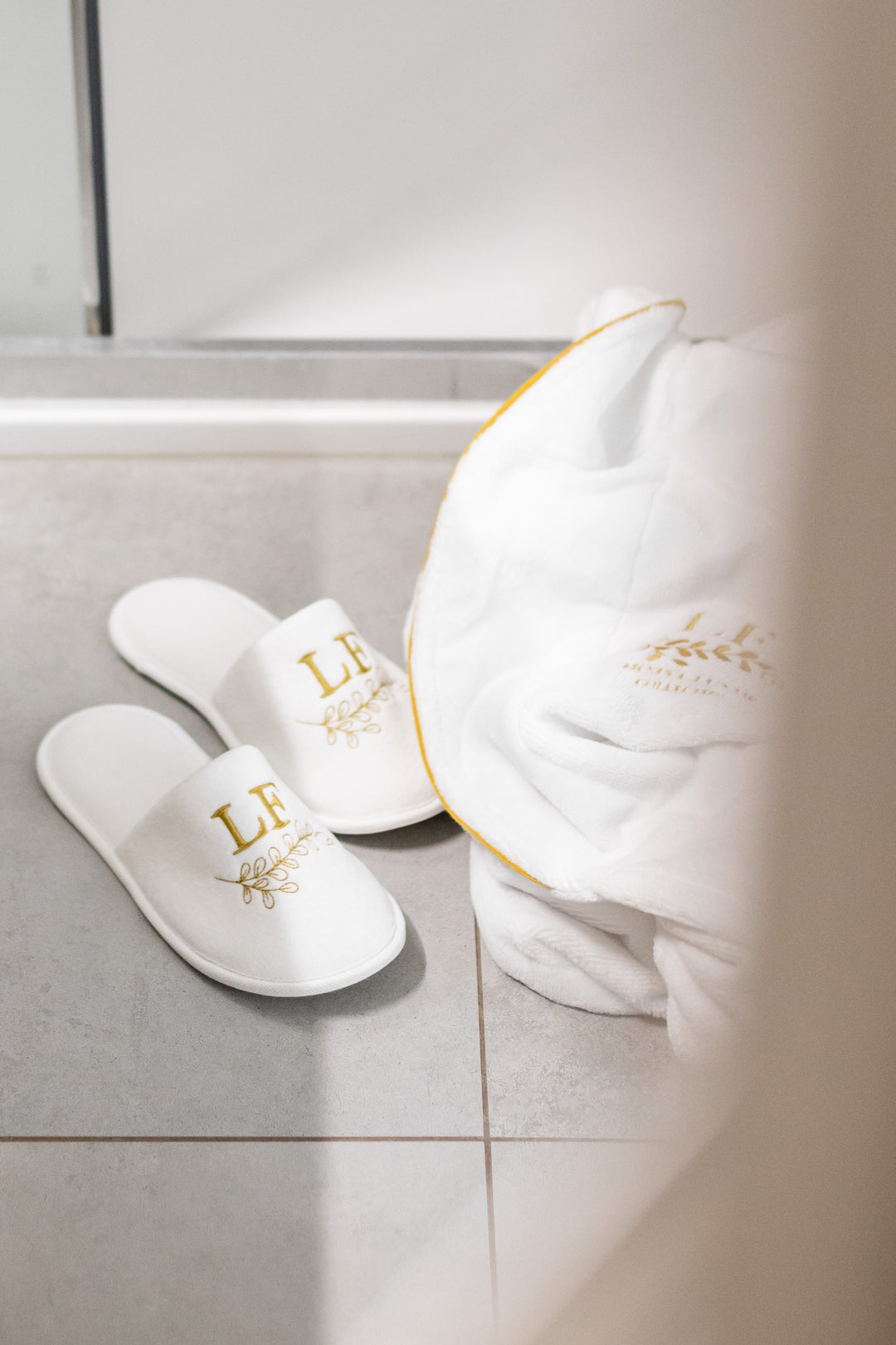 Valkoiset Loffen Hotel Luxus -kylpytossut ja kylpytakki harmaalla kylpyhuoneen lattialla