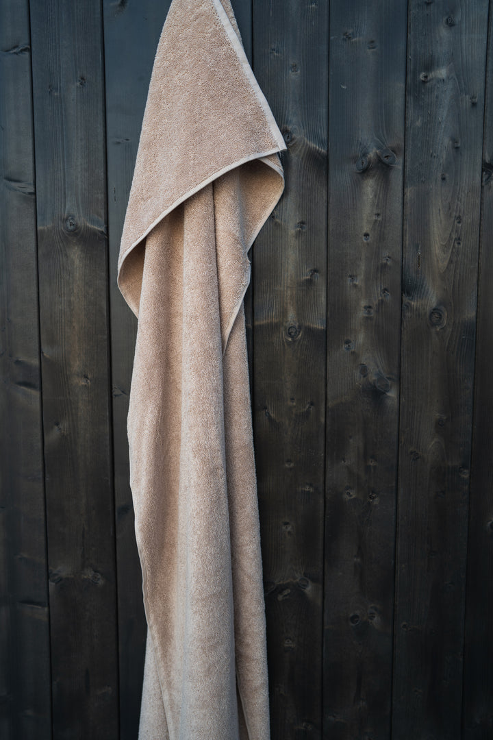 Beige Luxury Line -pyyhe riippumassa puuseinällä