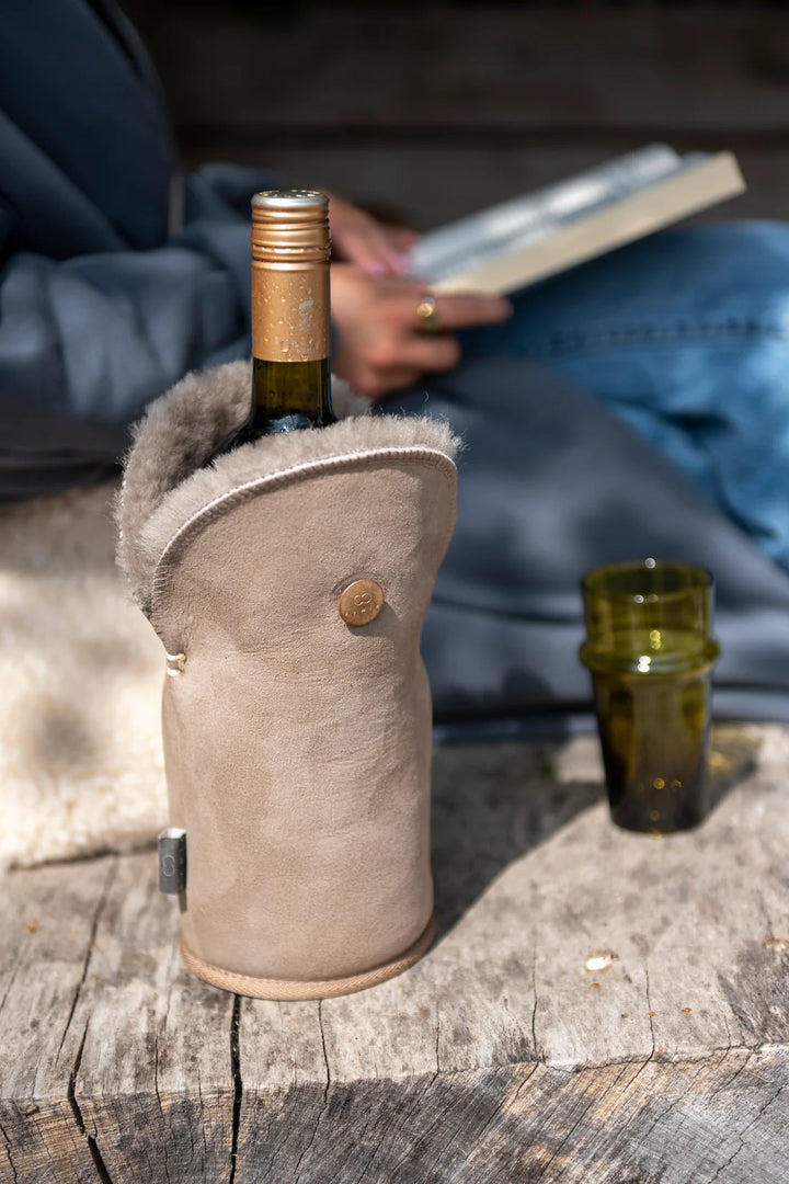 Harmaanbeige Kywie-viinicooler puisella alustalla, taustalla henkilö lukee kirjaa